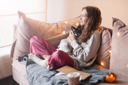 Morning, leisure, Christmas, winter and people concepts - happy young woman with cat and cup of coffee or tea in a cozy living room. Female at homeの写真素材