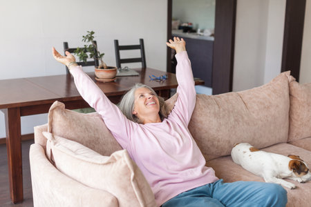 Portrait happy healthy middle aged woman relaxing on comfortable couch at home. Smiling pleasant 50s elderly gray-haired female with dogの写真素材