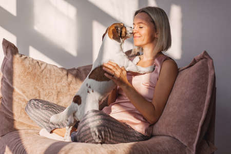 Middle-aged woman spends the weekend at home. Smiling female plays with her beloved dog while...