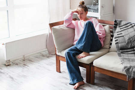 Unhappy depressed teenage girl sit on couch at home suffer from school bullying or discrimination, sad teen outcast feel lonely have difficulties with communication, puberty conceptの写真素材