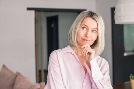 Attractive Middle aged woman smiling at the camera at home. Happy 40s lady thinking with hand on...