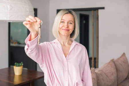 Headshot portrait of excited female happy winner buyer renter tenant of new home apartment. Middle-aged woman proud homeowner looking at camera showing keys of modern flatの写真素材