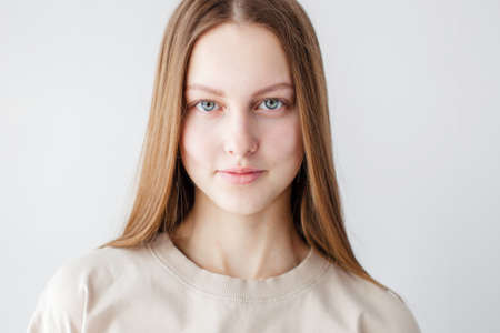 Close-up of cute teen girl smiling thoughtful at camera, standing over white background. Young generation Z woman in a beige T-shirtの写真素材