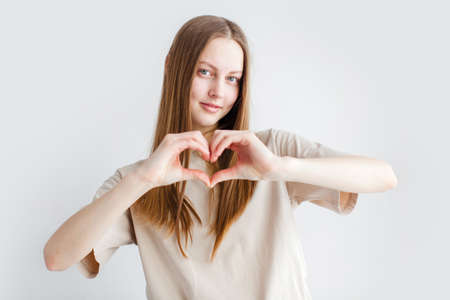 Beautiful young woman over a gray background Teen girl showing a heart shape with her handsの写真素材