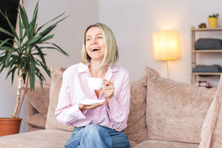 Adult woman sitting on the sofa at home and having a cup of coffee, relaxation concept