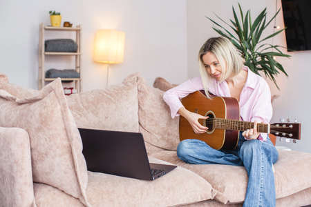 Middle aged woman practicing and learning how to play guitar on laptop computer monitor. Female guitarist watching online tutorialの写真素材