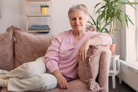 Cheerful senior female wearing pink formal blouse expressing joy, feeling happy and relaxed, sitting...