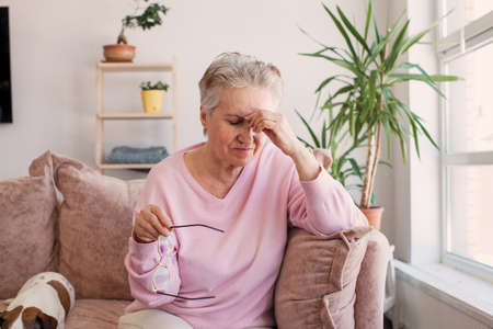 Pensive thoughtful middle aged lady looking away sit alone at home feel anxious lonely, sad depressed melancholic old mature woman suffer from sorrow grief thinking of problem suffer from solitudeの写真素材