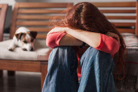 Teenage girl is worried about bullying. Sad young woman depressed sitting at home on the couch. Abuse or domestic violenceの写真素材