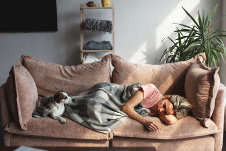 Frustrated, sad middle-aged woman is lying on couch at home. Depressed woman is lying in living room covered with blanketの写真素材