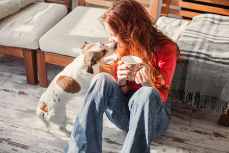 Young beautiful woman holding cup of coffee, sitting at home, Happy girl drinking tea, Teen girl with dogの写真素材