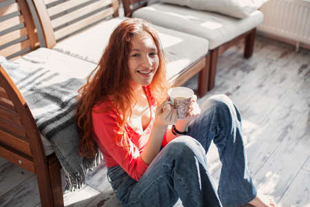 Happy young woman sitting on sofa in cozy clothes with cup of coffee or tea. Smiling teen at cozy home, top viewの写真素材