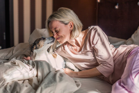 Positive middle aged relaxed woman with dog lying down and staying at home, daydreaming, napping, looking away, enjoying day off in bedの写真素材