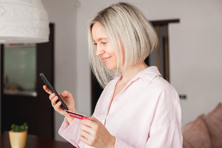 Safe mobile banking. Smiling middle aged lady clienthold mobile phone credit bank card do online shopping providers internet payment. Happy adult woman enjoy easy fast secure transfer money in bank appの写真素材