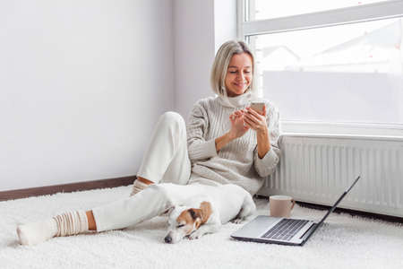 Attractive middle-aged freelance woman works on a laptop and talks on the phone from home. Lady works at a remote jobの写真素材