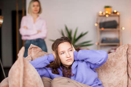 Angry mom scolds her teen daughter at home. Girl ignoring her mom. Troubled teenage child and her mother are quarrellingの写真素材