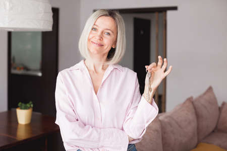 Happy middle aged woman customer landlord hold key to new house apartment give to camera, older retired female hand real estate owner make sale purchase property deal concept, close up viewの写真素材