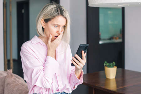 Portrait of depressed middle-aged woman feel upset and sad after phone call, bad news in social media or smart phone messenger online app. Frustrated beautiful female sit in depression alone on sofa at homeの写真素材