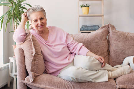 Happy woman relaxing on her couch at home in the living room. Portrait of beautiful mature woman...