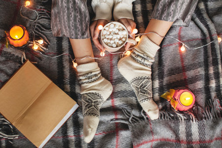 Soft photo of woman on the bed with cup of coffee in hands, top view point. Cozy autumn or winter home concert. female in warm socksの写真素材