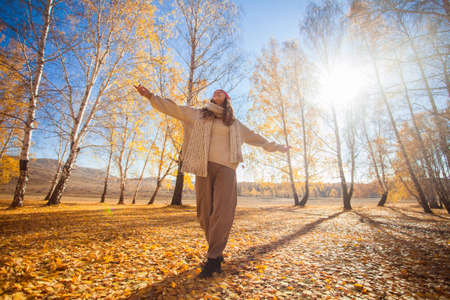 Portrait of funny young woman in the autumn weather in warm clothes and hats. Happy teenage girl walks in the park, enjoys the yellow autumn leaves in fallの写真素材