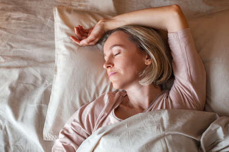 Pretty middle aged woman sleeping on bed in modern apartment. Female in bedroom at homeの写真素材