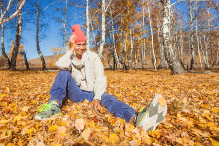 Happy adult woman enjoy walking in autumn forest. Middle aged lady dressed in warm sweater and hat walks on a sunny day in fallの写真素材