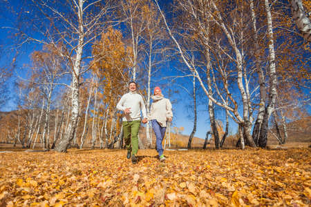 Middle age Couple wearing in autumn-style clothes running through the autumn landscape. Alley covered with yellow foliage. Fall walk outdoors. Two lovers in autumn park. romantic datingの写真素材