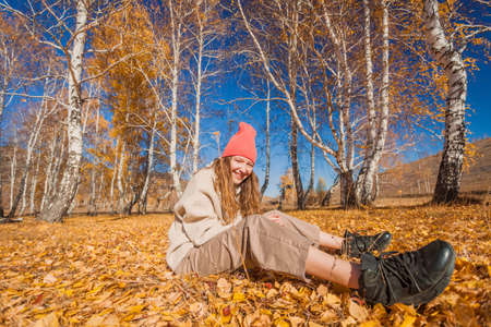 Portrait of funny young woman in the autumn weather in warm clothes and hats. Happy teenage girl walks in the park, enjoys the yellow autumn leaves in fallの写真素材