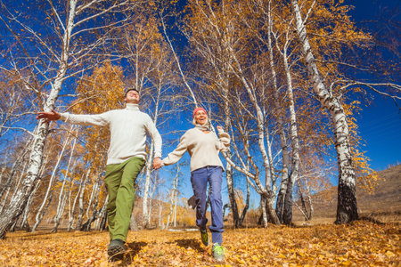 Middle age Couple wearing in autumn-style clothes running through the autumn landscape. Alley covered with yellow foliage. Fall walk outdoors. Two lovers in autumn park. romantic datingの写真素材