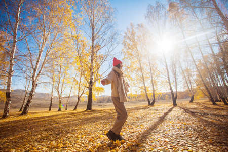 Young cheerful woman walks in autumn park. Teenage girl in orange hat plays with yellow leaves in the forest, full lengthの写真素材