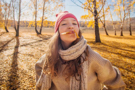 Young cheerful girl walks in autumn park. Teenage girl in orange hat plays with yellow leaves in the forestの写真素材