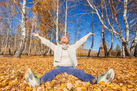 Middle aged woman walking in autumn park. Lady in orange hat plays with yellow leaves in the forestの写真素材