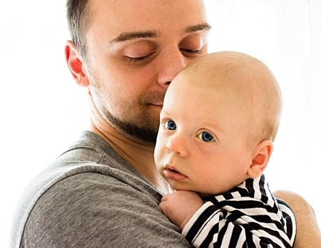 A little baby in a striped shirt in the arms of his father, looks thoughtfully