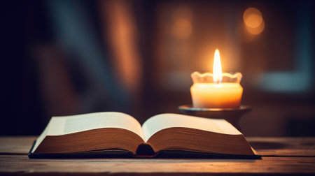 An open book lies next to a glowing candle on a wooden table, creating a serene atmosphereの素材