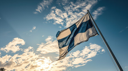 Finnish flag fluttering against a sunny blue sky with cloudsの素材