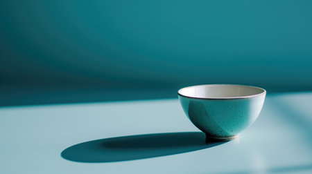 Elegant turquoise bowl on a blue surface with a pronounced shadowの素材