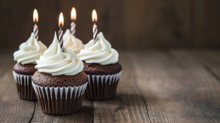 Chocolate cupcakes with lit candles on a wooden backdropの素材