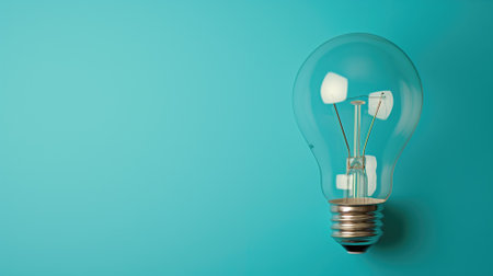 Single incandescent light bulb standing against a turquoise-colored backgroundの素材