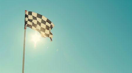 Checkered flag waving against clear blue sky with sun flareの素材