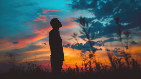 Silhouette of man standing in field at sunset, gazing colorful skyの素材