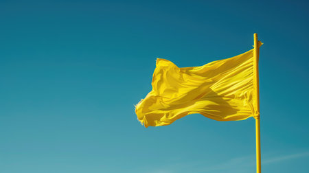 Bright, yellow flag waving in clear blue skyの素材
