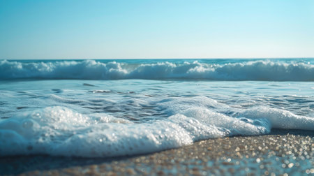 Gentle ocean waves rolling onto sandy beach under bright blue skyの素材
