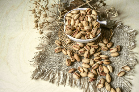 Salty pistachios in ceramic cup with thorns and marble stones on rough gray clothの写真素材