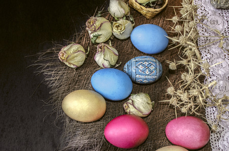 Easter eggs with dry rose buds and thorns on the openwork strip with a straw rug on the black...