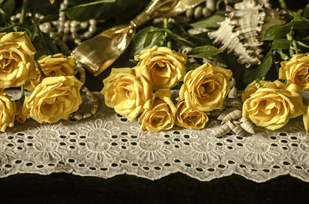 Sprigs with yellow roses, dry branches of white gypsophila,reeds on a white lace border with beads pearls, seashells and golden ribbon on a black backgroundの写真素材