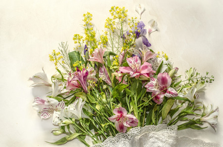 Delicate background of wild herbs with white and pink flowers of Alstroemeria and purple iris with openwork border on light plywoodの写真素材