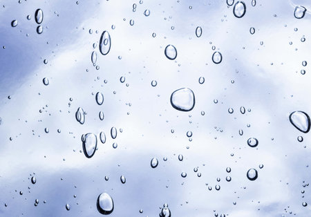Water drops on glass with blue sky background. Rain drops on window.の写真素材