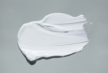White thick cream smudge swatch textured gray colored background. Baby skin care or zinc mask.