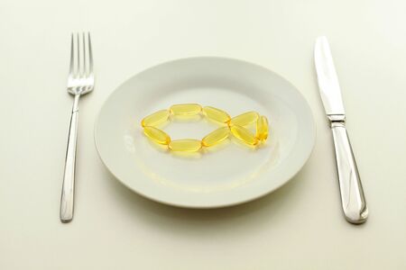 fish from omega 3 capsules on a white plate with a fork and knife on the sides of the plate